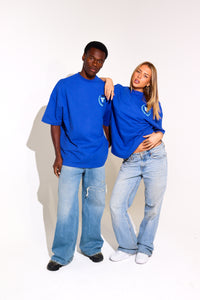 Two people wearing matching blue t-shirts and jeans against a plain background